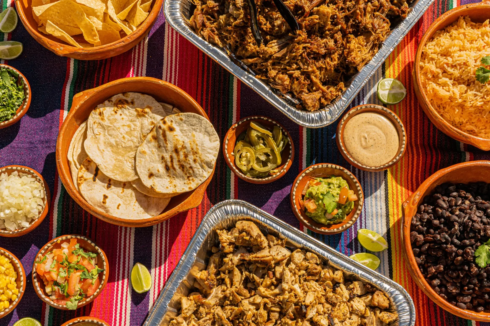 Charolas de carnitas, pollo, arroz, frijoles, tortillas y salsas